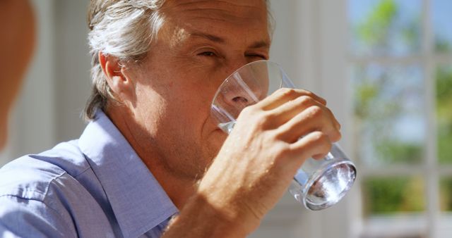 A middle-aged Caucasian man is drinking a glass of water, with copy space. His expression suggests he might be quenching his thirst or taking a moment to relax.
