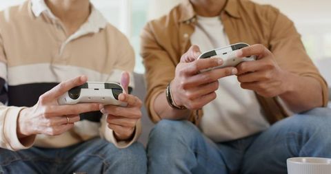 Friends playing video games with white wireless controllers on couch in cozy living room
