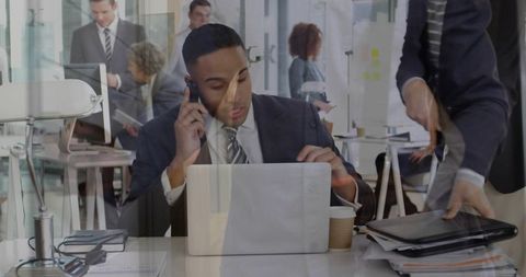 Executive juggling phone and laptop in modern open-plan office, multitasking
