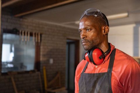 Experienced african american craftsman wearing safety gear while working in industrial woodworking s