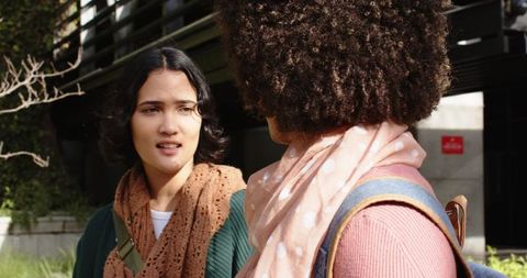 Two students talking on college campus courtyard wearing knit scarves and backpacks