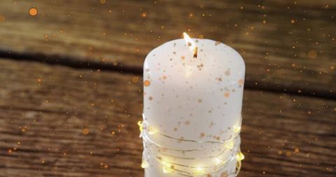 Glowing white pillar candle wrapped in fairy lights on rustic wood with gold bokeh ambience