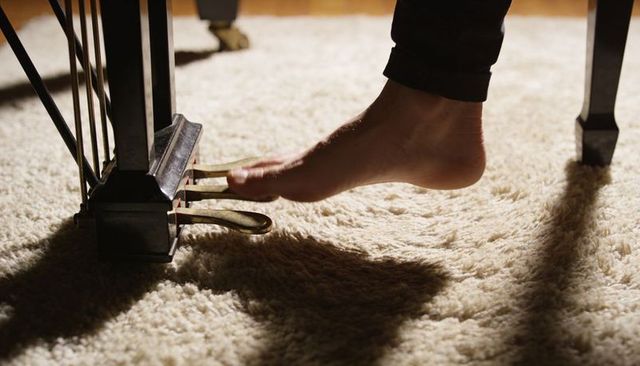 Pressing bare foot on grand piano pedal on plush carpet, warm cozy living room close-up