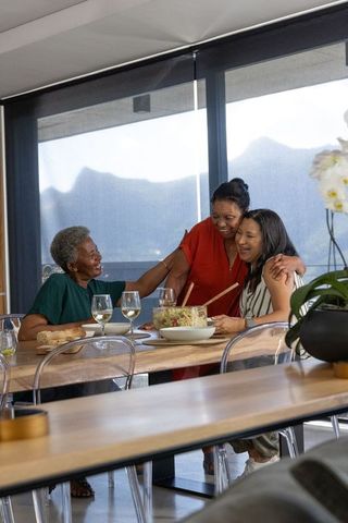 Multigenerational african american women hugging and smiling around wooden dining table with salad