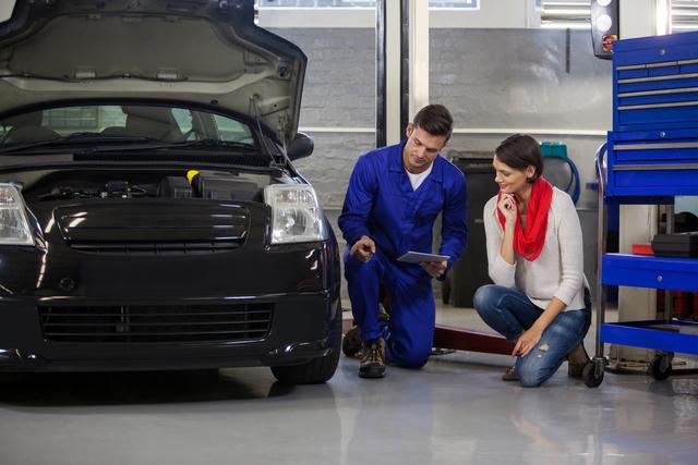 Mechanic in blue overalls showing female customer issues with her car in a repair garage. Useful for automotive industry promotions, customer service training materials, and illustrating professional car maintenance services.