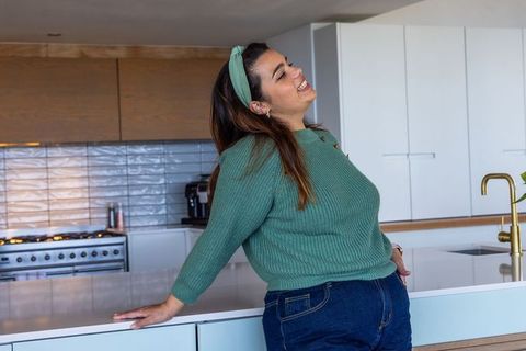 Laughing woman leaning on kitchen island wearing green sweater in modern bright kitchen