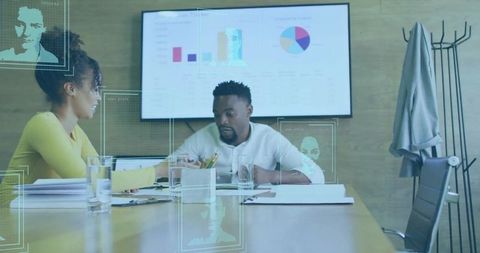Two professionals collaborating over reports and charts in boardroom with holographic data overlay