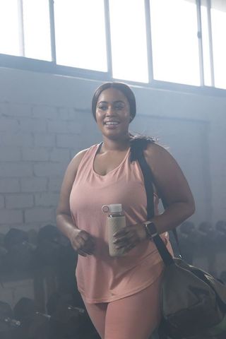 Plus size african american woman smiling carrying gym bag holding reusable bottle