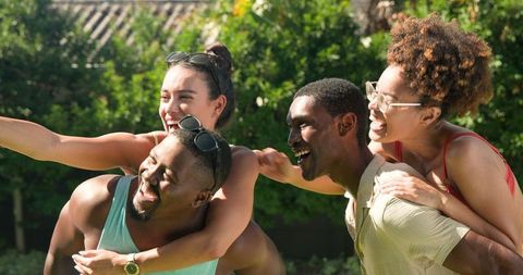 Diverse friends enjoying piggyback rides in garden laughing together