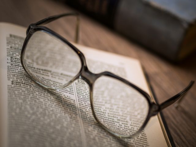 Reading glasses resting on open book with blurred text emphasize focus on reading and learning. Ideal for education, libraries, studying, book-related promotions, and eye care themes. Use this for articles on literature, academic materials, and scholarly studies.