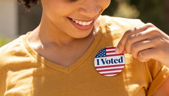 Smiling woman pinning i voted sticker on mustard shirt close-up sunny outdoor portrait