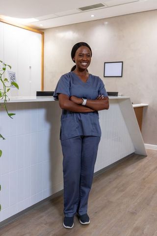 African female nurse standing at clinic reception smiling wearing scrubs and smartwatch