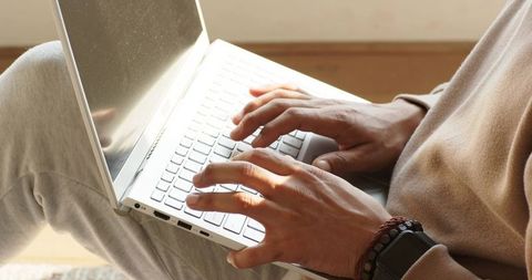 Man typing on laptop in cozy daylight wearing smartwatch and beaded bracelet