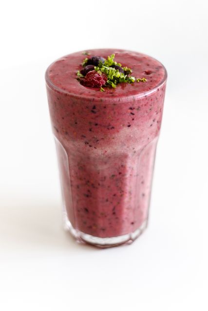This vibrant and nutritious mixed berry and leafy green smoothie is served in a clear glass, highlighting its rich color. Ideal for promoting healthy eating, fitness, and wellness, this image can be used in food blogs, nutrition articles, recipe books, and juice bar menus.