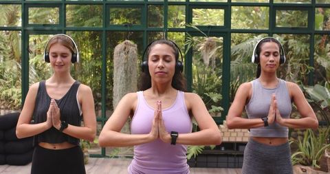 Women Meditating with Headphones in Tranquil Greenhouse
