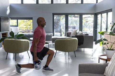 Senior Man Doing Kettlebell Lunges in Modern Living Room with Large Windows
