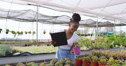 Woman Examining Succulent in Greenhouse with Clipboard