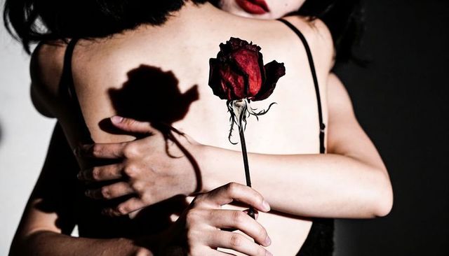 Holding dried red rose while hugging, moody high-contrast embrace with rose shadow