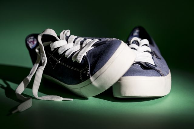 A close-up view of classic blue canvas sneakers with white laces, showcased on a green background. Ideal for use in fashion promotions, online stores specializing in footwear, sports equipment advertisements, and lifestyle blogs discussing casual wear.