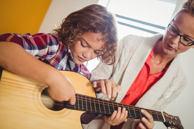Boy learning how to play the guitar with the help of a teacher