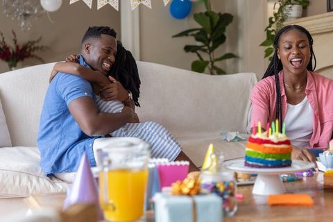 African american family celebrating birthday at home with rainbow cake and gifts