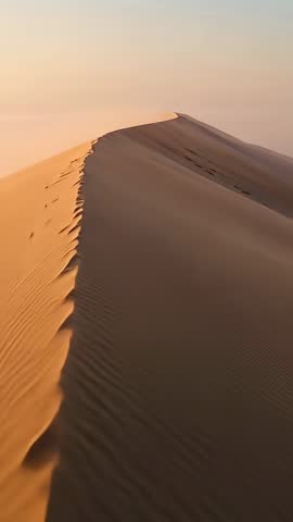 Sliding camera along dune crest at golden hour revealing ripples and footprints