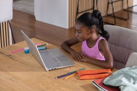 Young girl studying on laptop at wooden table at home, remote learning focus