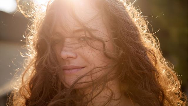 Backlit woman with flowing curly hair at golden hour, sunlight glowing lens flare portrait
