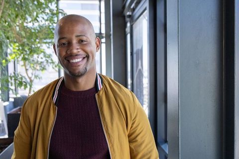 African american man smiling by office windows wearing mustard jacket and maroon sweater