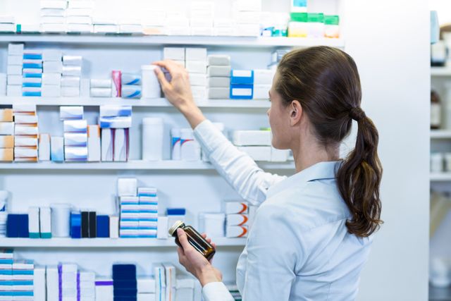 Pharmacist organizing medicine on shelves in a pharmacy. Ideal for use in healthcare, pharmaceutical, and medical-related content. Can be used in articles about pharmacy operations, healthcare professionals, and medication management.