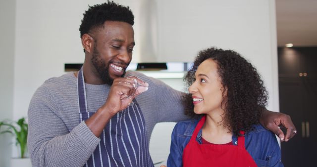 Happy african american couple wearing aprons, using tablet in kitchen and talking. family time, having fun together at home.