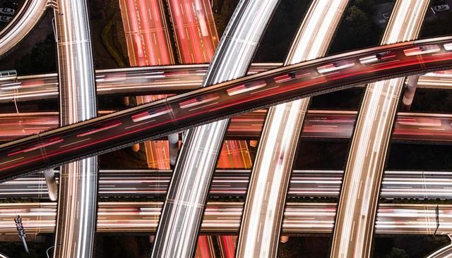 Aerial long-exposure multilayer highway interchange pulsing with red and white light trails