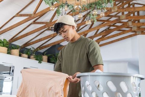 African young man folding shirt in bright farmhouse kitchen with wooden beams and plants