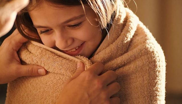 Smiling child wrapped in cozy towel after bath with caring adult hands