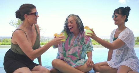 Women clinking drinks by infinity pool celebrating friendship on sunny poolside retreat