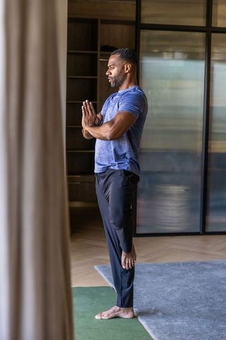 Mature african american man practicing tree pose on green mat in modern home studio daily