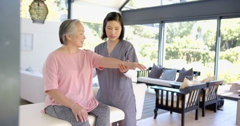 Physiotherapist guiding senior asian woman with home arm exercises