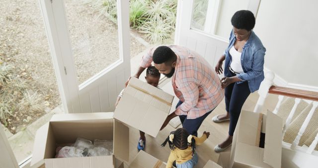 Young African American family with children is unpacking moving boxes in their new home. Parents and kids are working together, making the move-in process exciting and joyful. This portrayal of a happy, modern family moving into a new house can be used for advertisements, real estate marketing, and content related to family, housing, or relocation.