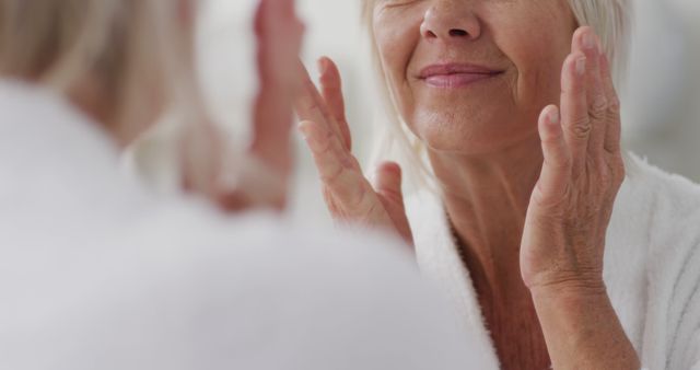 Happy senior caucasian woman looking at mirror in bathroom and touching her face - Download Free Stock Photos Pikwizard.com