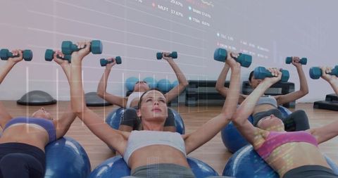 Group fitness class performing chest presses on stability balls with dumbbells