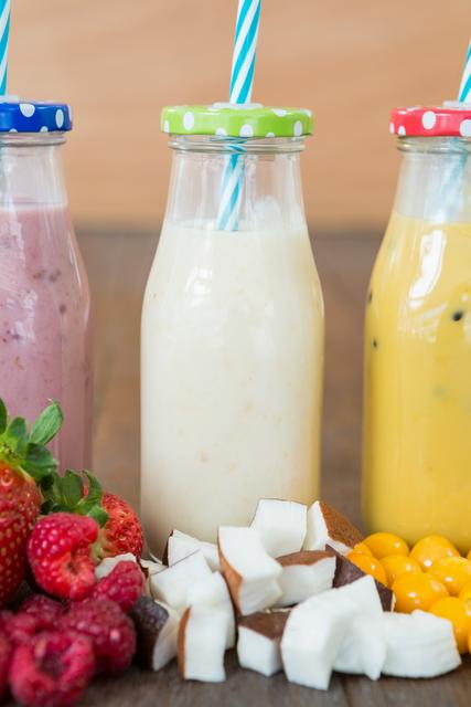 Three bottles with smoothie and fresh chopped fruits on wooden board