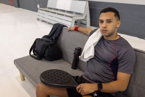 Pickleball player resting on bench with paddle and water bottle, wearing smartwatch