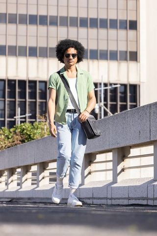 African american man walking on urban bridge wearing sunglasses carrying black messenger bag