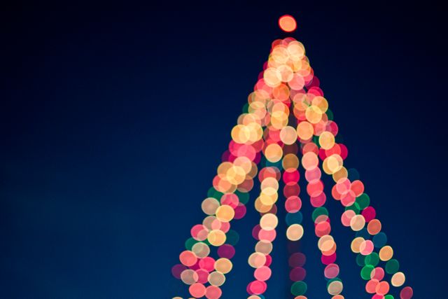 Image captures colorful, blurred Christmas tree lights against a dark blue background, perfect for holiday cards, festive promotions, advertisements, website banners, and social media posts during the holiday season.