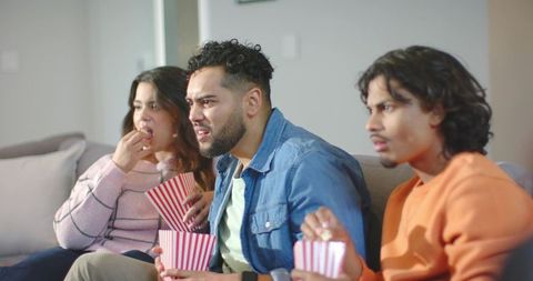 Friends watching tense movie on couch sharing popcorn during cozy night
