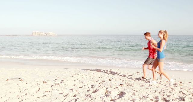 Couple enjoying morning jog along sandy beach, promoting fitness and healthy lifestyle. Ideal for health-related campaigns, outdoor activity promotions, travel brochures, and summer destination advertisements.