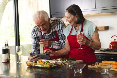 Senior couple cooking together using tablet recipe in modern kitchen