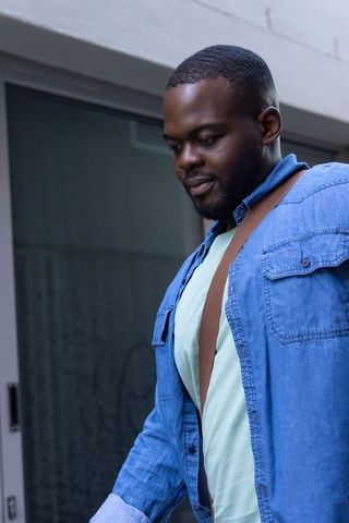 African american man commuting in denim shirt carrying brown strap at urban entrance