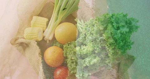 Rustic summer produce flatlay with kale, corn, scallions, citrus and tomato on burlap