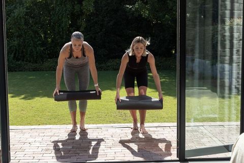 Two middle-aged women rolling yoga mats on sunny backyard patio together preparing for workout